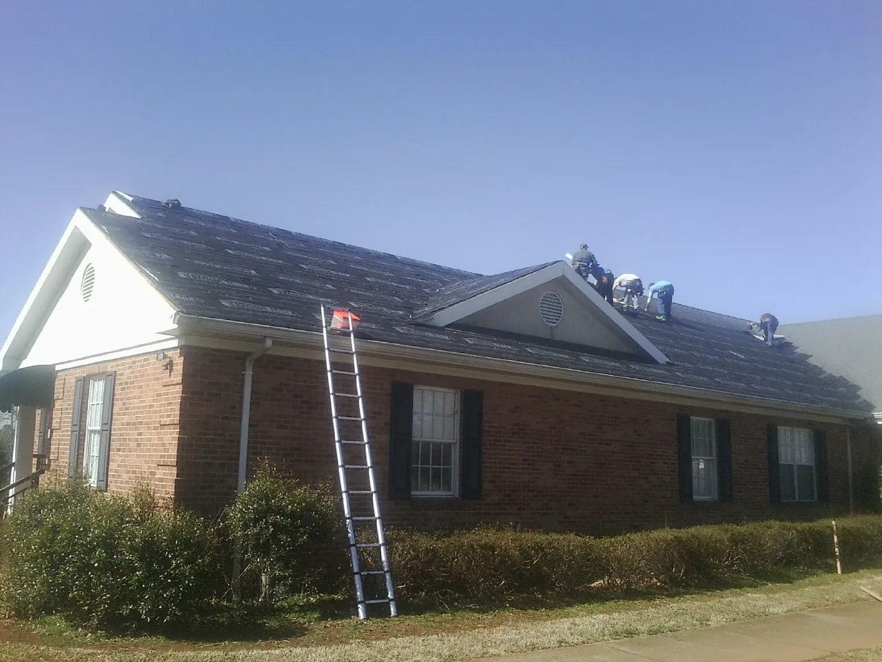 Crew tearing shingles off a brick ranch roof with a ladder set — Emergency Roof Repair work by our crew in Filley