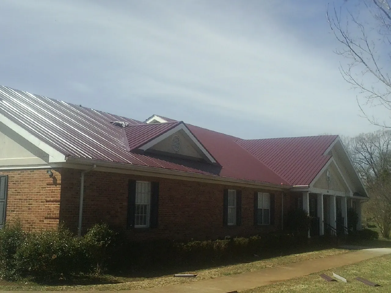 Red metal roof with gabled entries on a long brick building, from a Hail Damage Roof Repair job in Filley