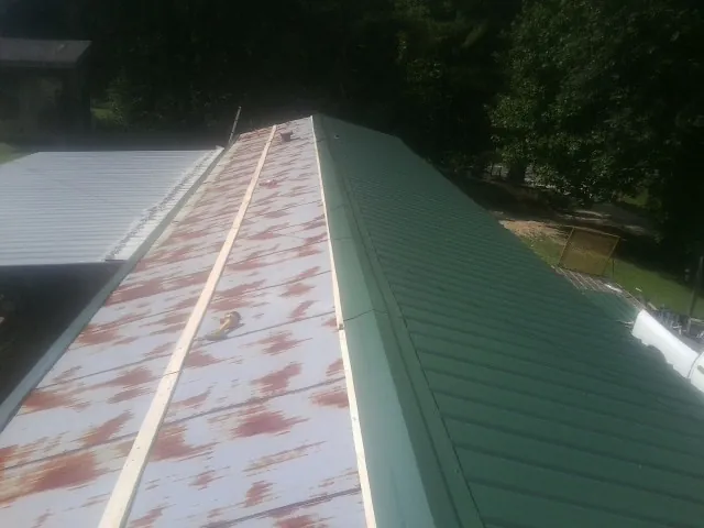 Old rusted panels beside newly installed green metal roofing — Wind Damage Roof Repair by Roofing Brothers in Filley