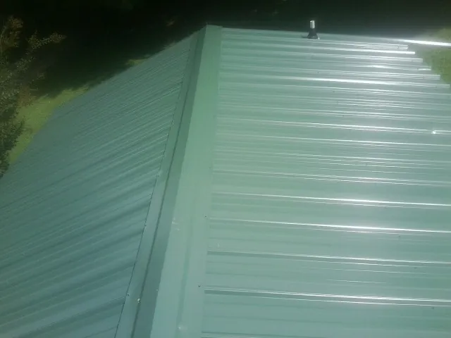 New green metal panels meeting at the ridge of a roof — Flat Roof Repair work by our crew in Filley
