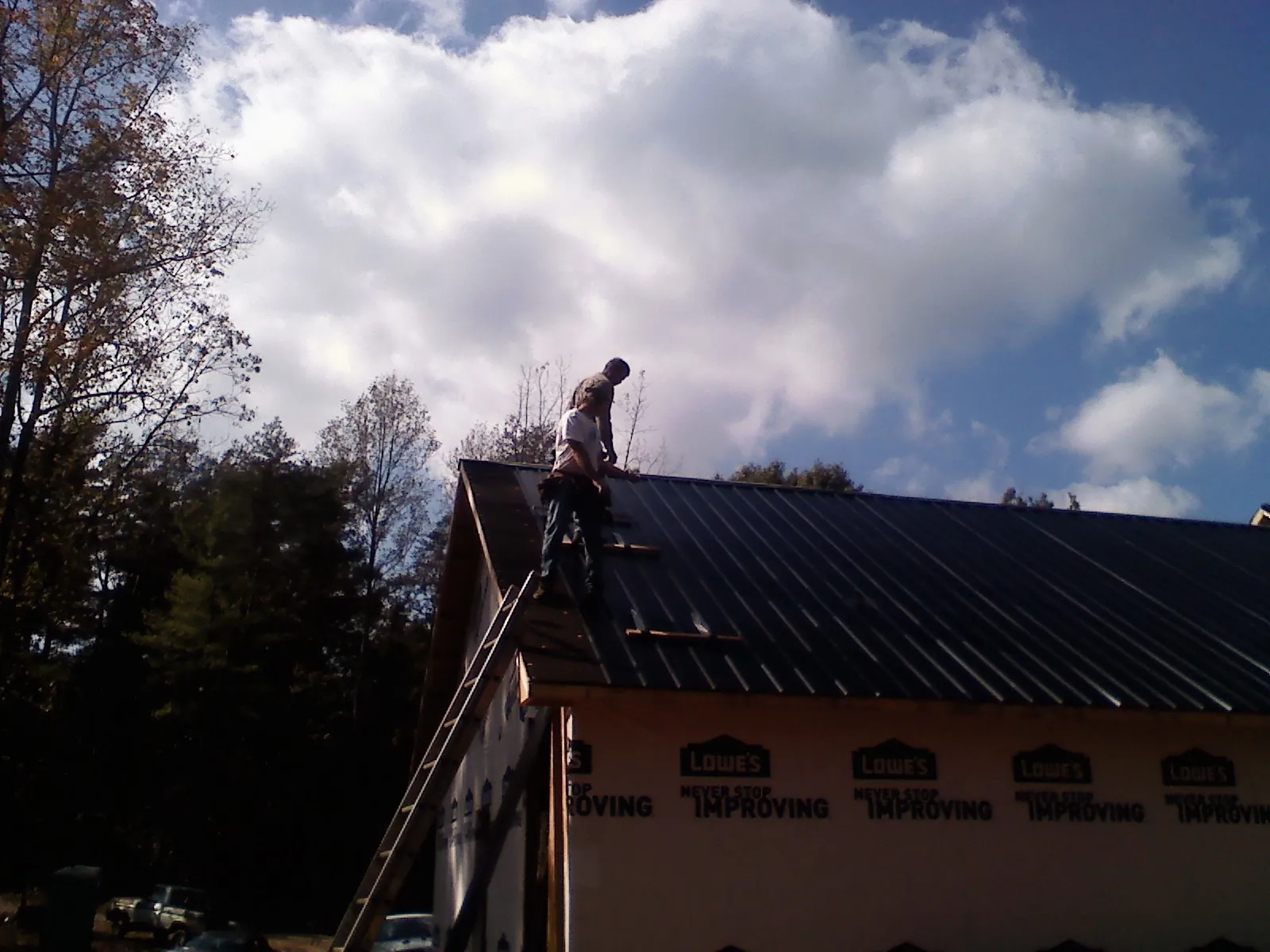 Roofer fastening dark metal panels high against a cloudy sky, from a Roof Inspection job in Filley