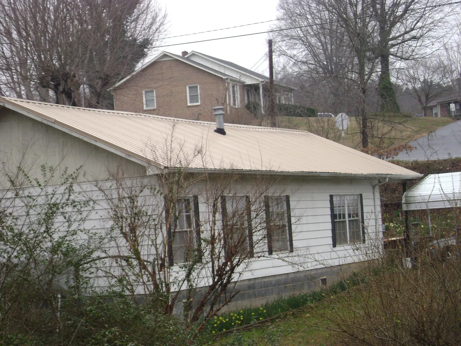 Tan metal roof on a white sided house set into a hillside — Commercial Roofing by Roofing Brothers in Filley